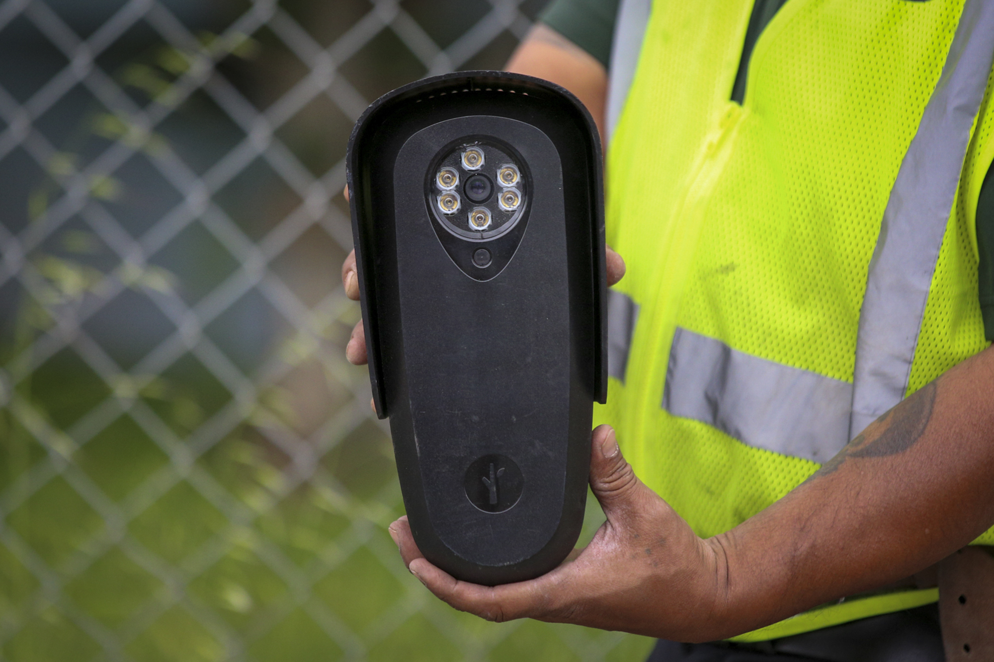 A worker in a high visibility vest holds up a black camera.