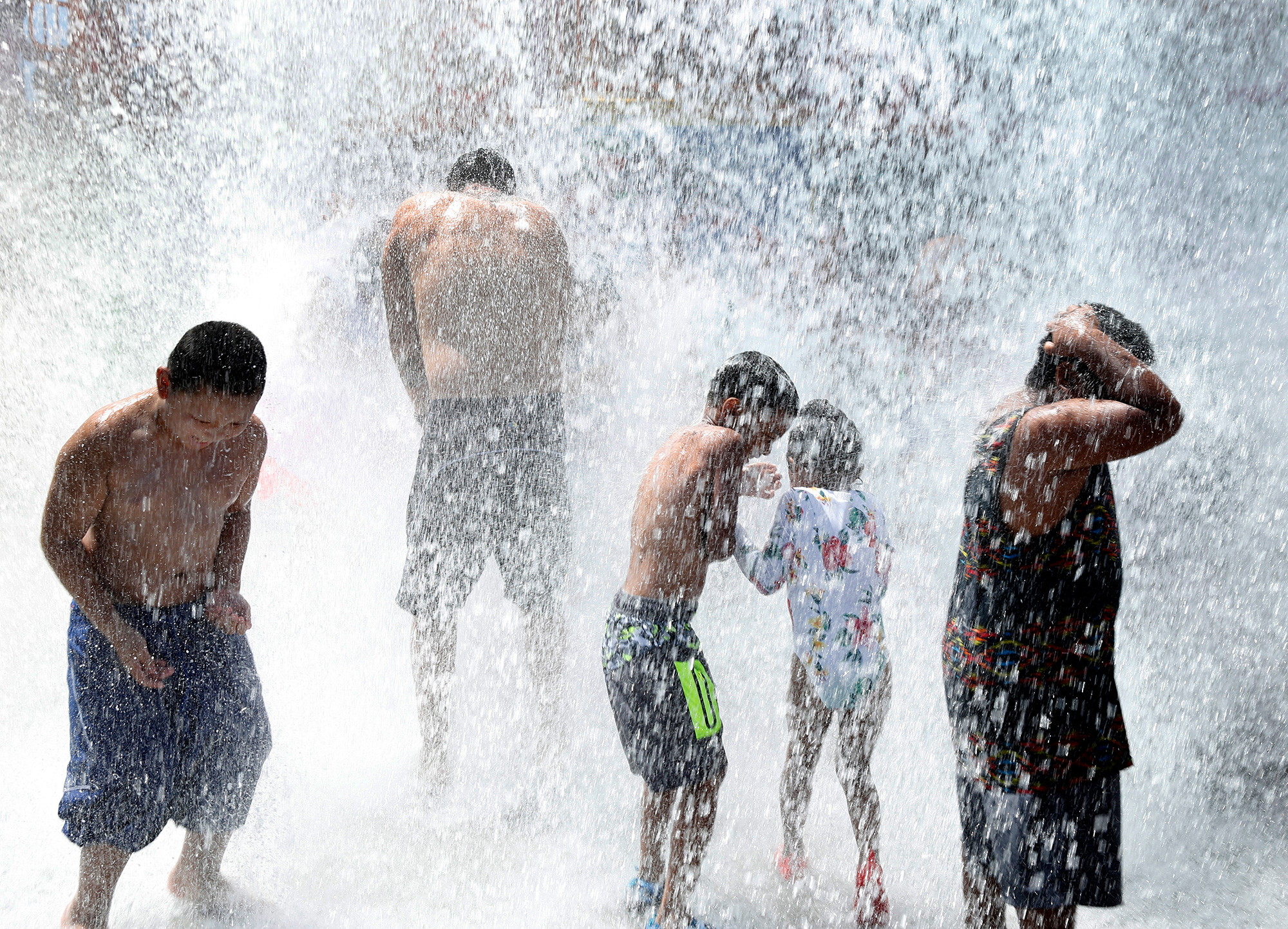 Young kids in swimwear getting soaked by falling water