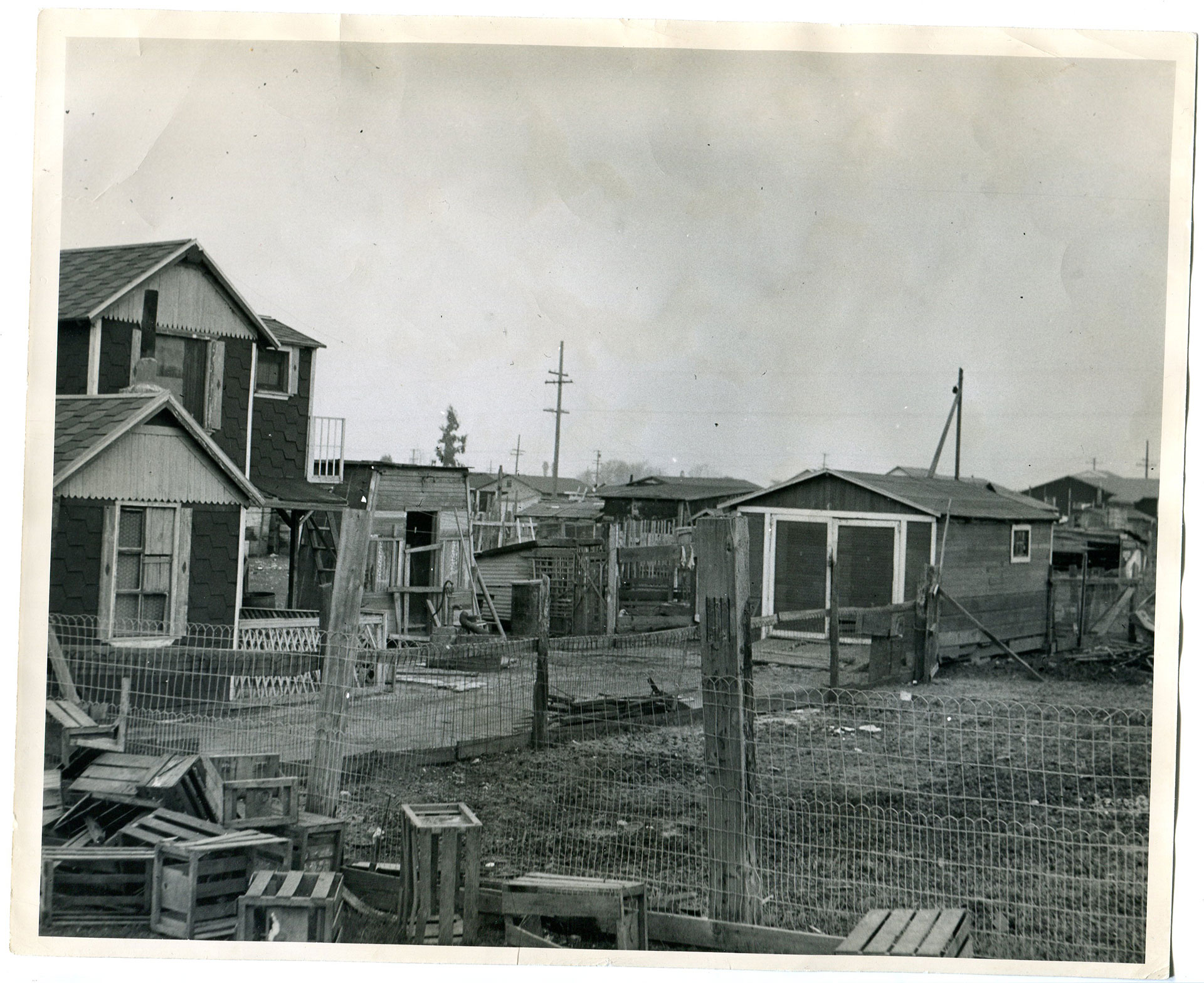 A black-and-white photograph of several wooden buildings, including a home, a large shed or garage and several small structures.
